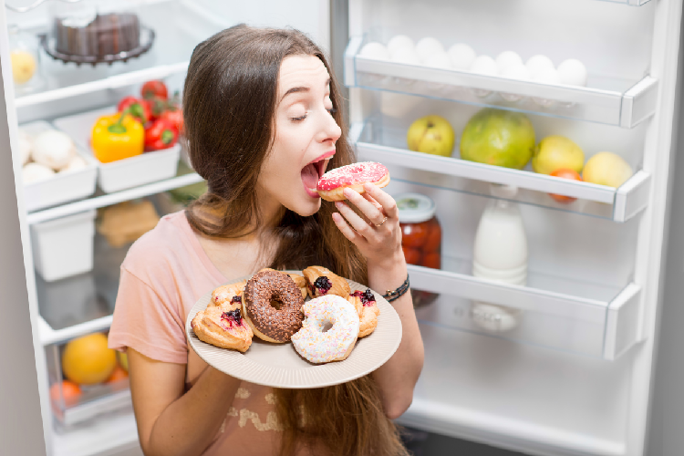 冷蔵庫の前でドーナツを食べる女性