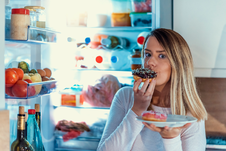 冷蔵庫の前でスイーツを食べる女性