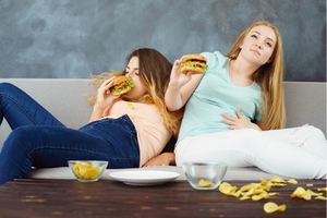 ハンバーガーを食べて苦しそうにする女性2人