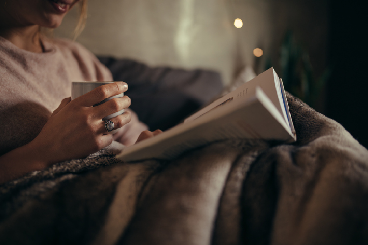 飲み物を片手にベッドで本を読む様子